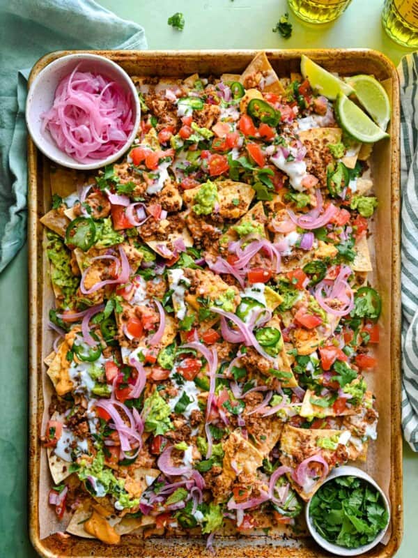 vegan nachos on a tray with pickled onions, lime wedges, and cilantro