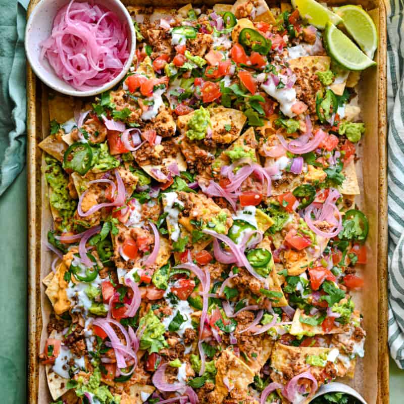 vegan nachos on a tray with pickled onions, lime wedges, and cilantro