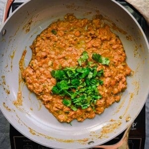 homemade refried beans in frying pan with chopped cilantro on top