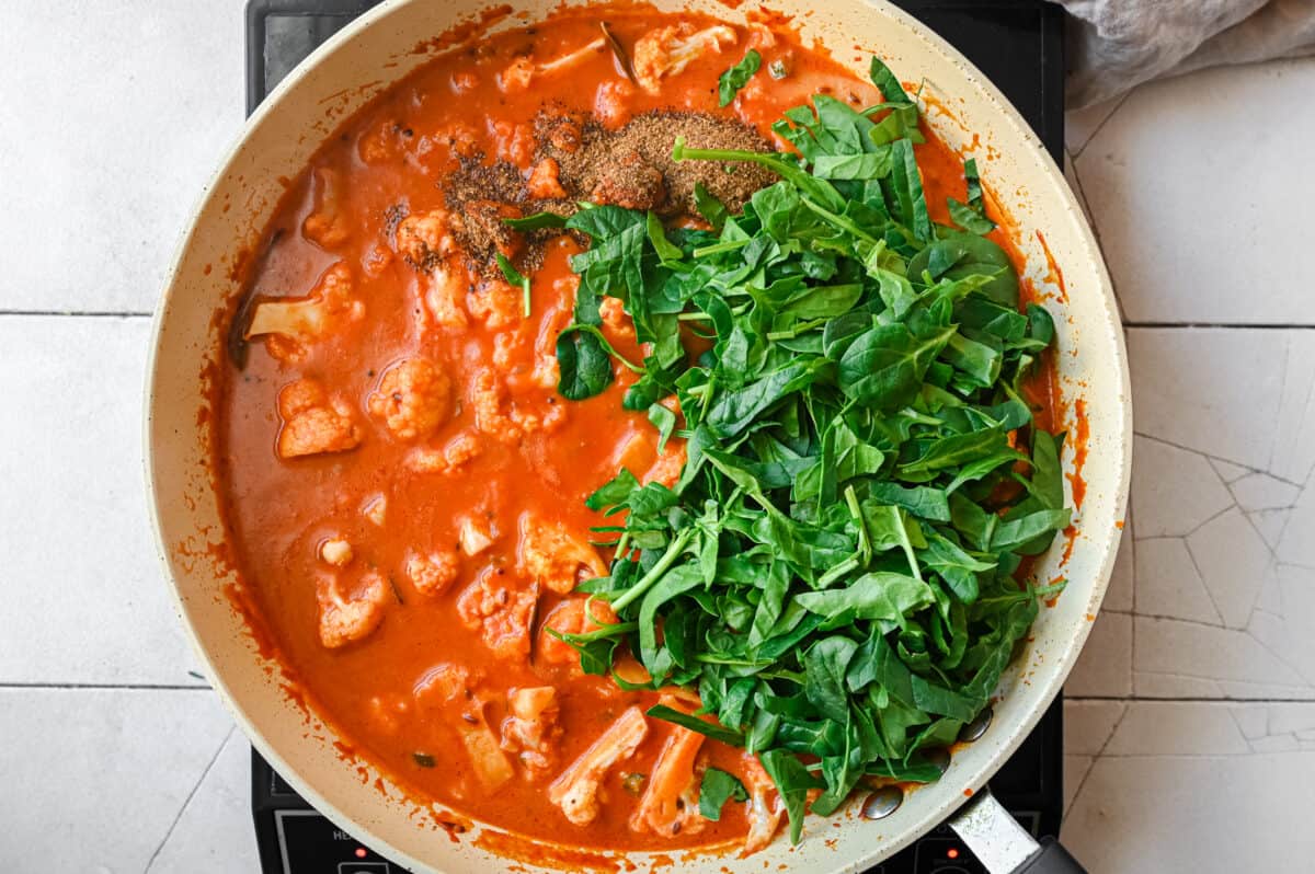 chopped baby spinach on top of a vegan cauliflower curry in a frying pan