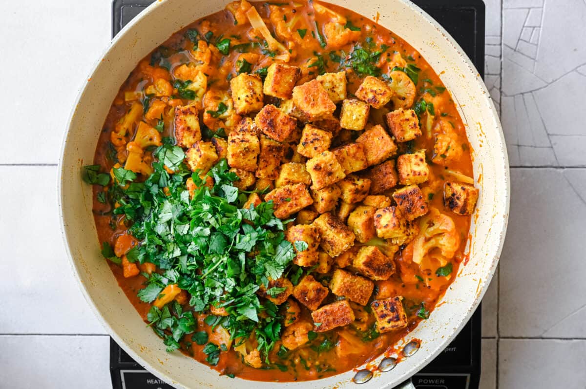 fried tofu and chopped cilantro on top of a vegan curry in a frying pan