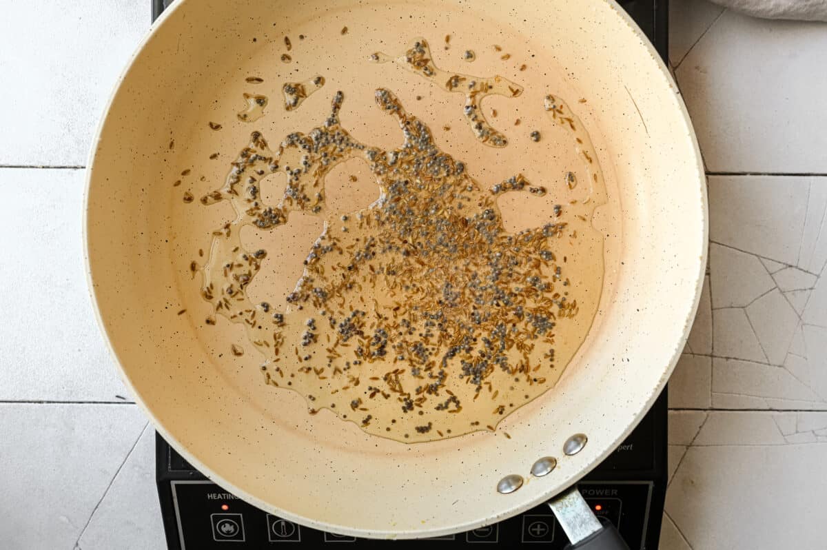 black mustard seeds and cumin seeds frying in oil in a frying pan