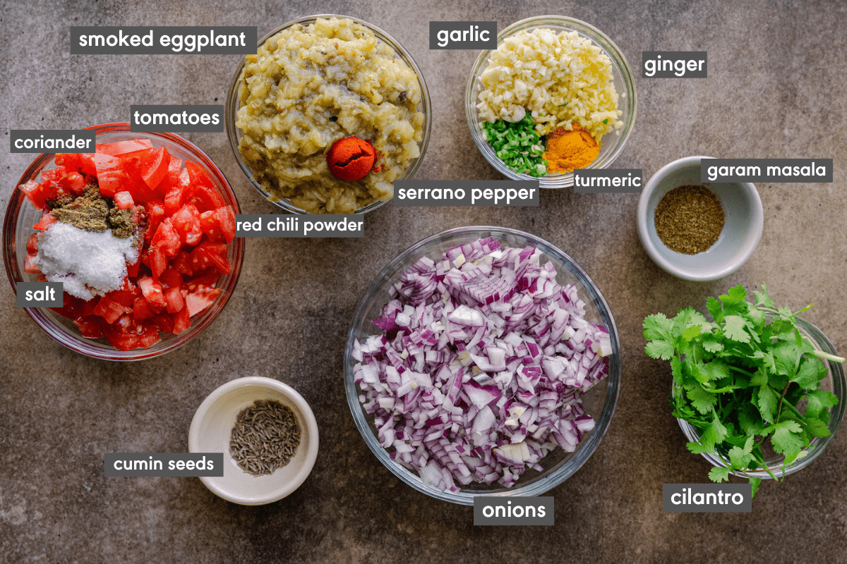 prepped ingredients for baingan bharta on brown surface, with ingredients labeled. 