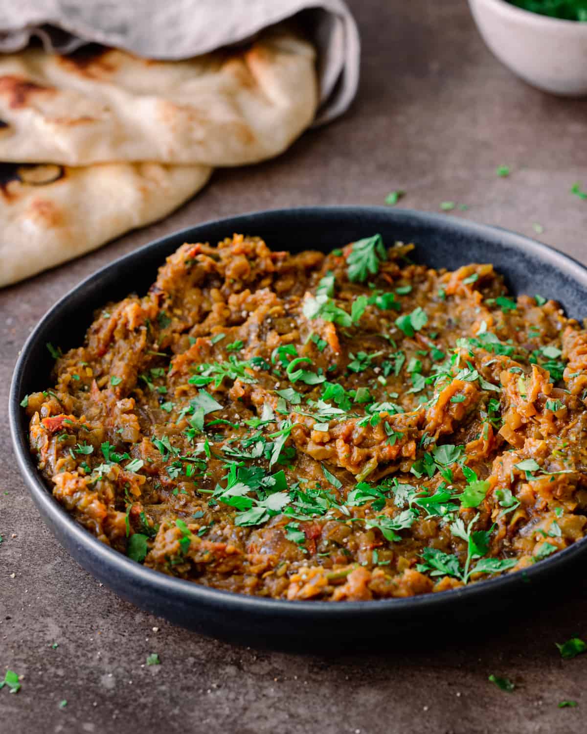 baingan bharta in a shallow dark bowl with naan in the background. 