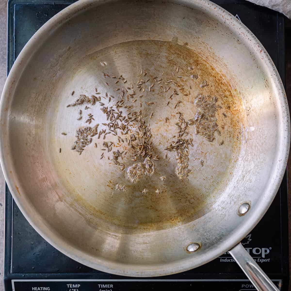 cumin seeds frying in oil in frying pan