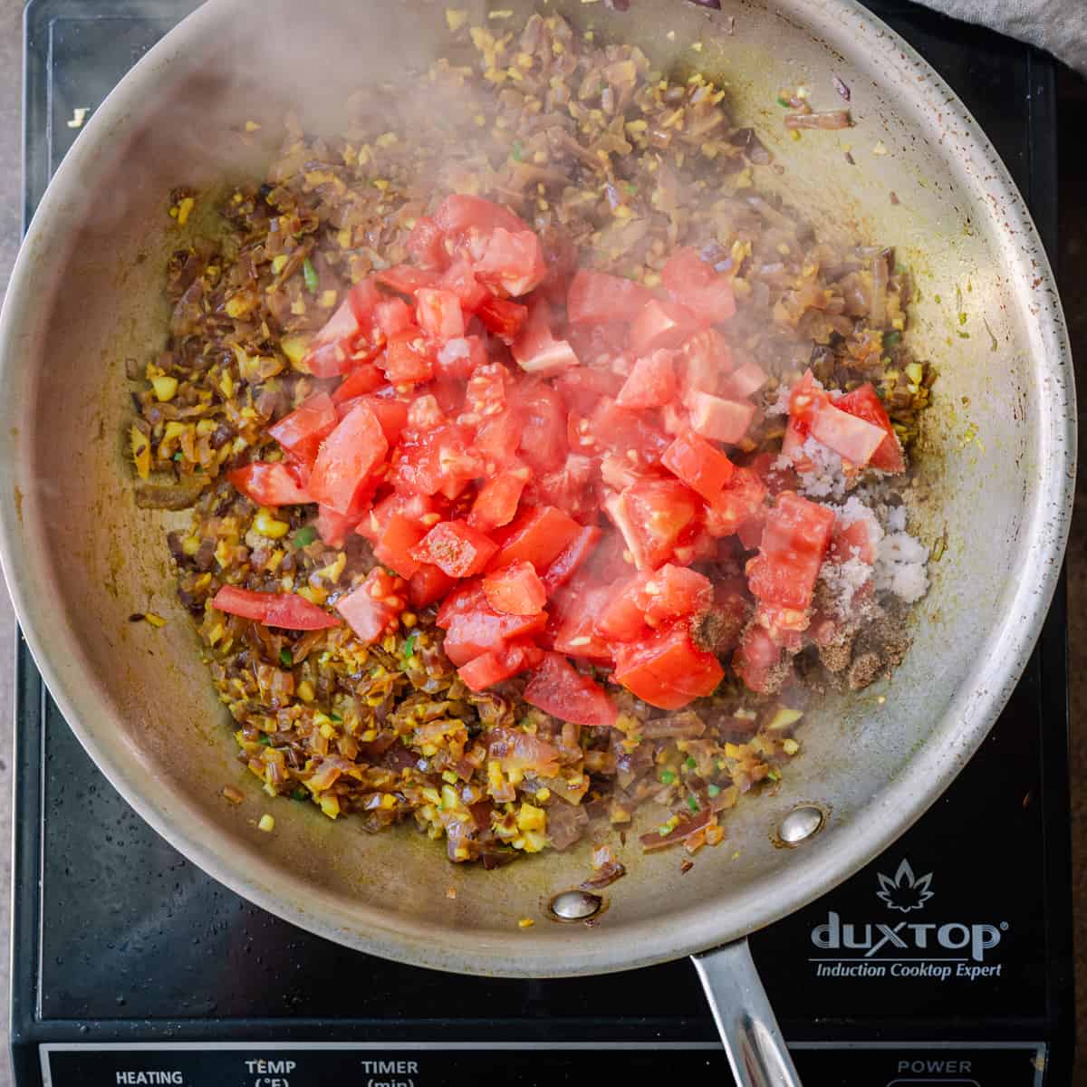 chopped tomatoes on top of indian masala frying in skillet