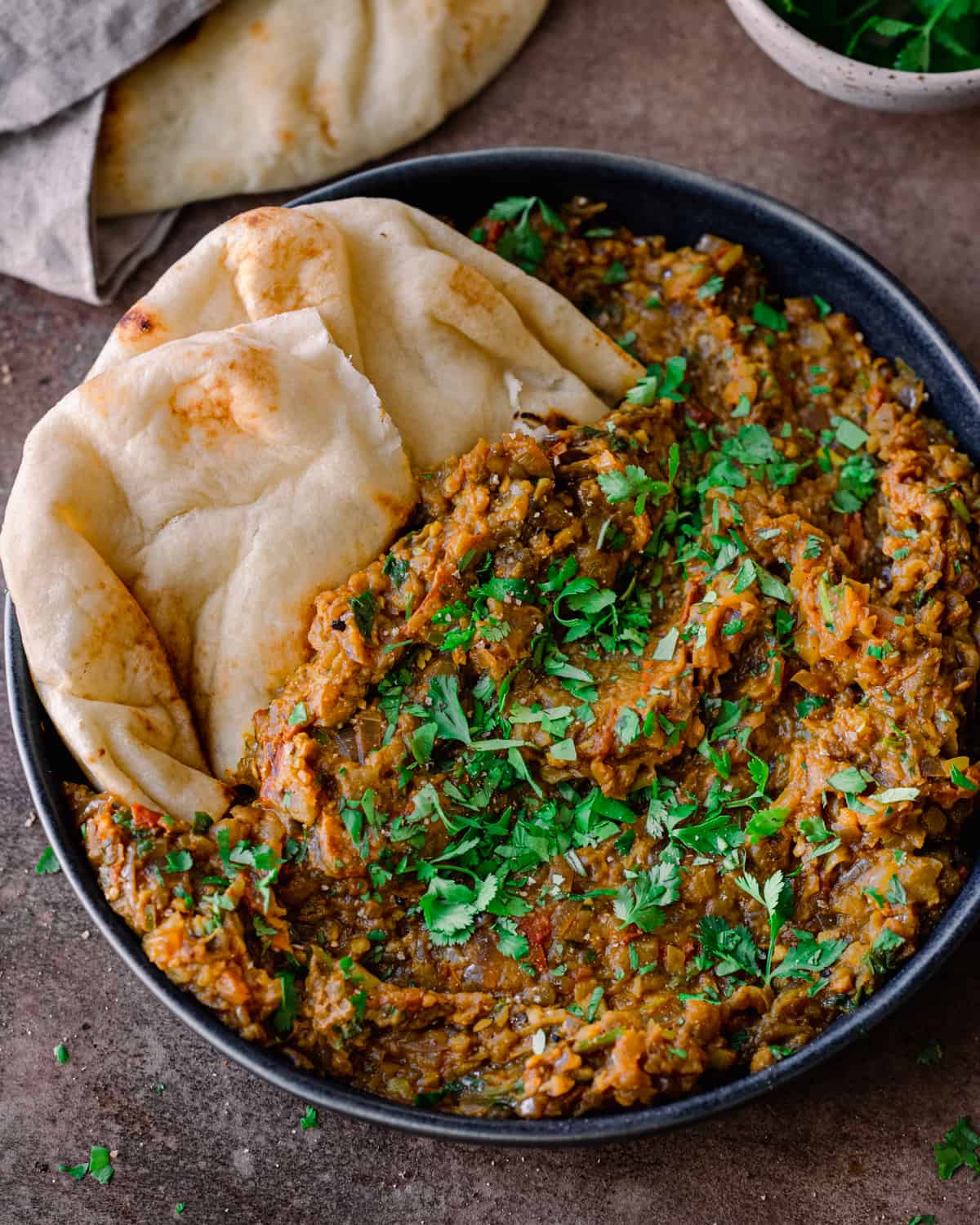 baingan bharta in a shallow bowl with naan dipped into the dish