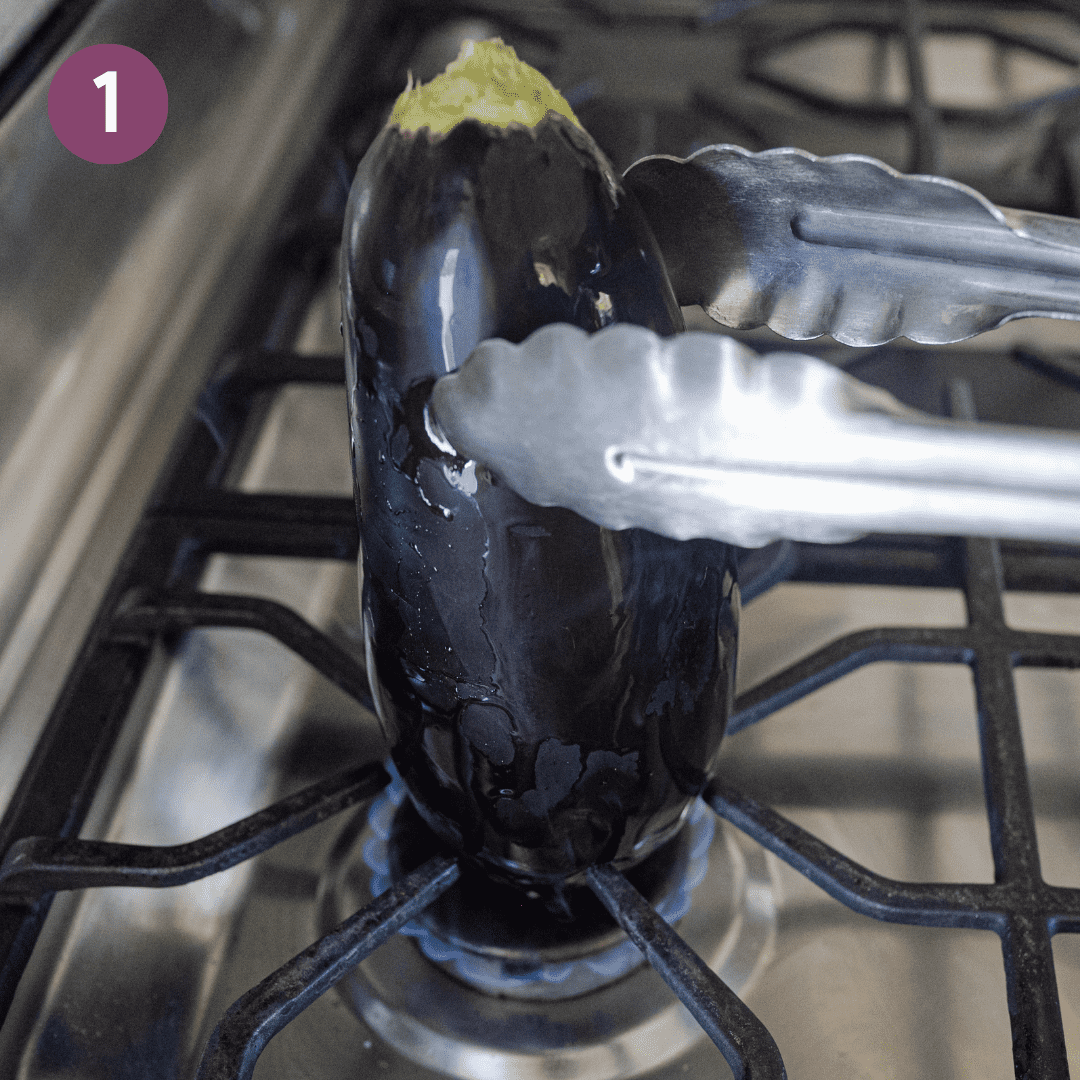 tongs holding up a whole eggplant over an open gas flame. 
