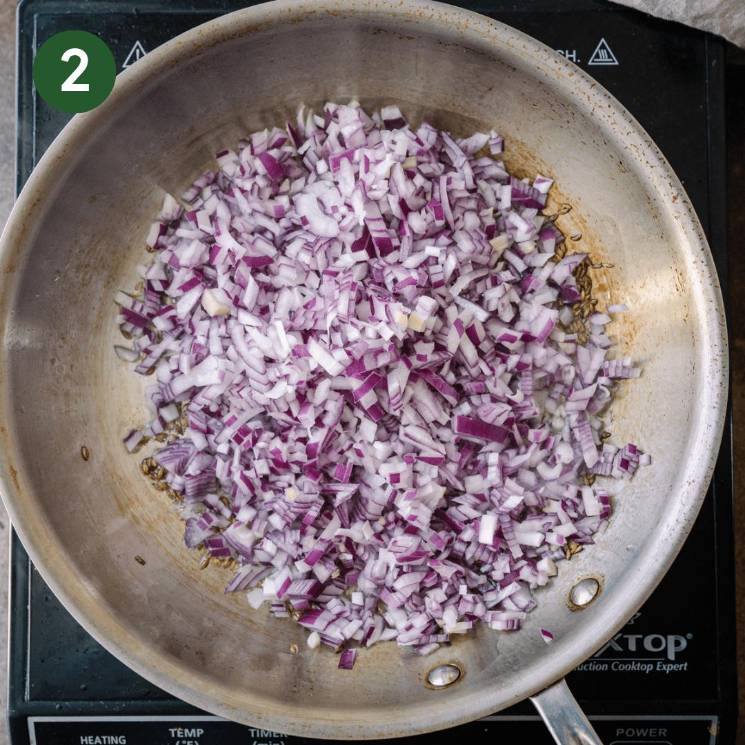 diced red onions frying in oil in a stainless steel skillet.