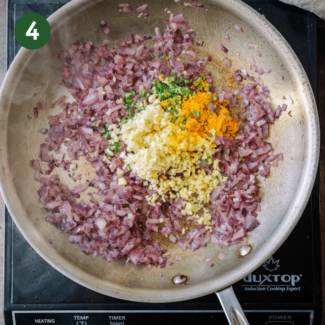 ginger, garlic, turmeric, and serrano peppers on top of frying red onions in skillet.