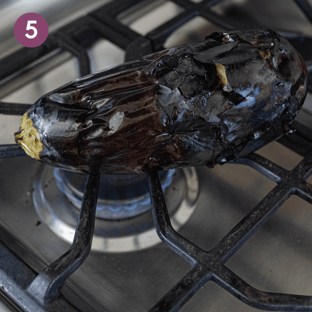 wrinkly, charred eggplant cooking on top of a gas flame on the stove.