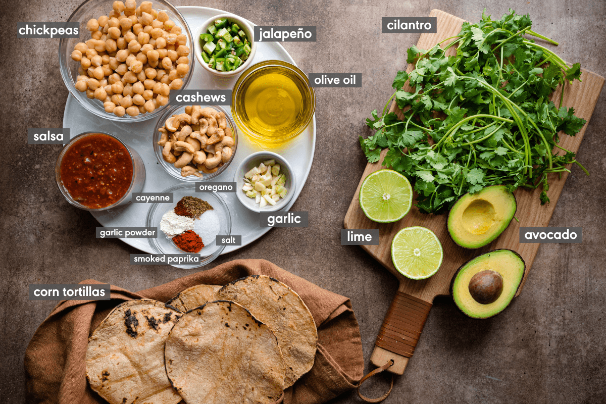 ingredients for chickpea tacos with corn tortillas on a brown board. 