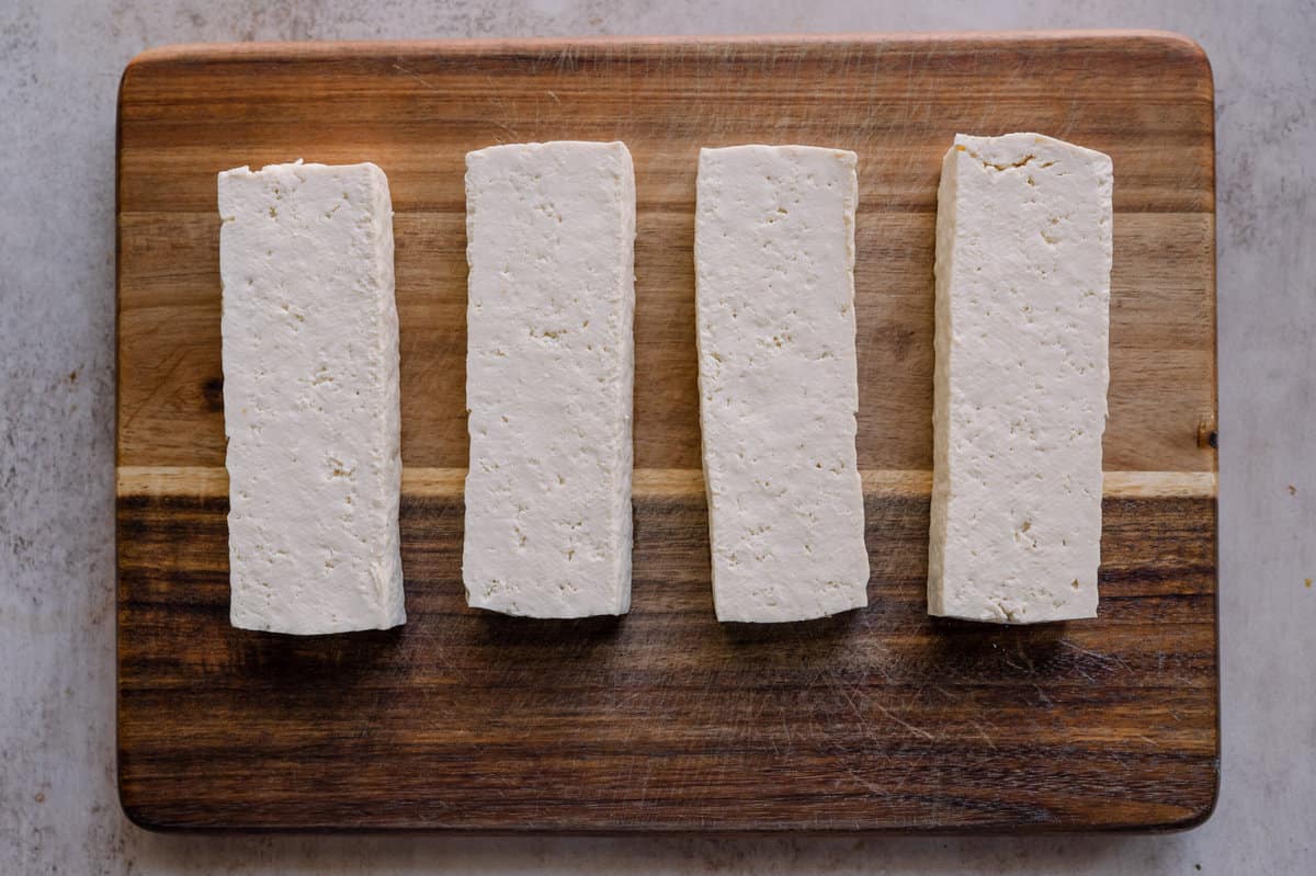 4 tofu slabs sitting on wooden cutting board.