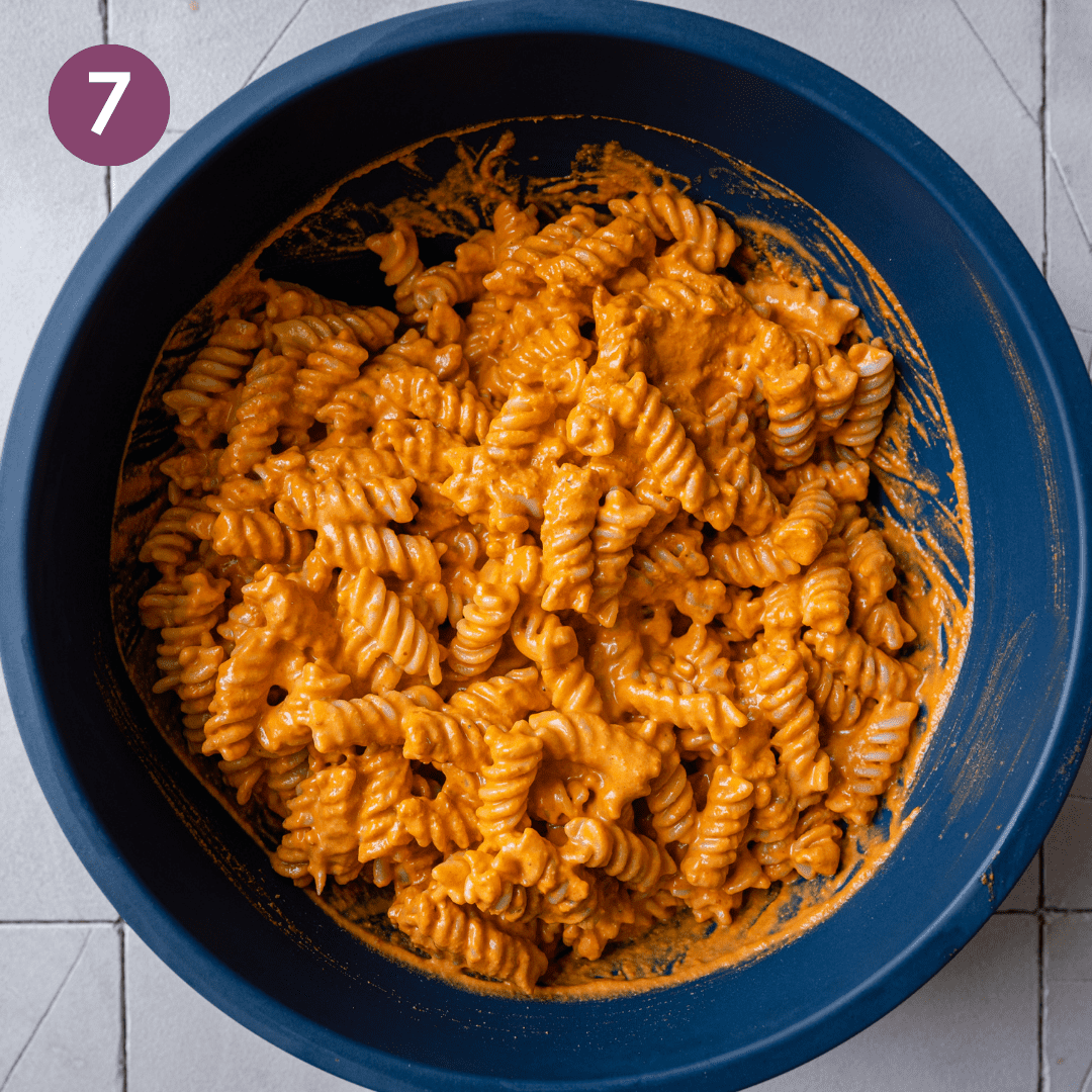 roasted red pepper sauce tossed into pasta in a big blue bowl.