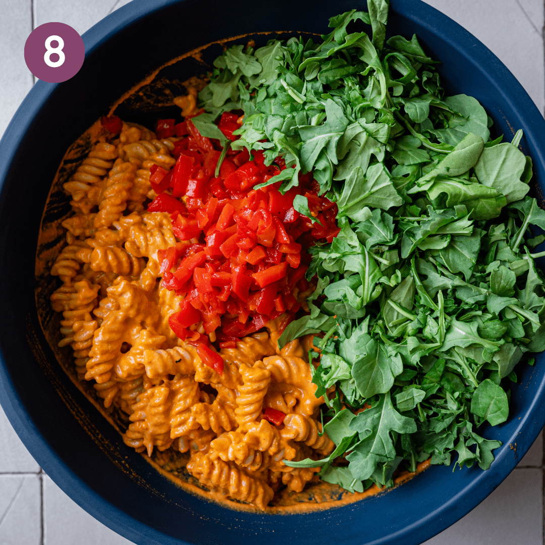 roasted red pepper pasta in blue bowl with chopped peppers and arugula.