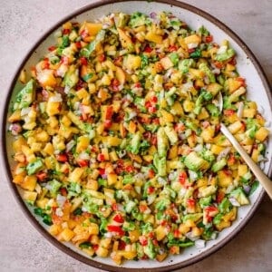 peach salsa with avocado and red onion in a white bowl with gold spoon.