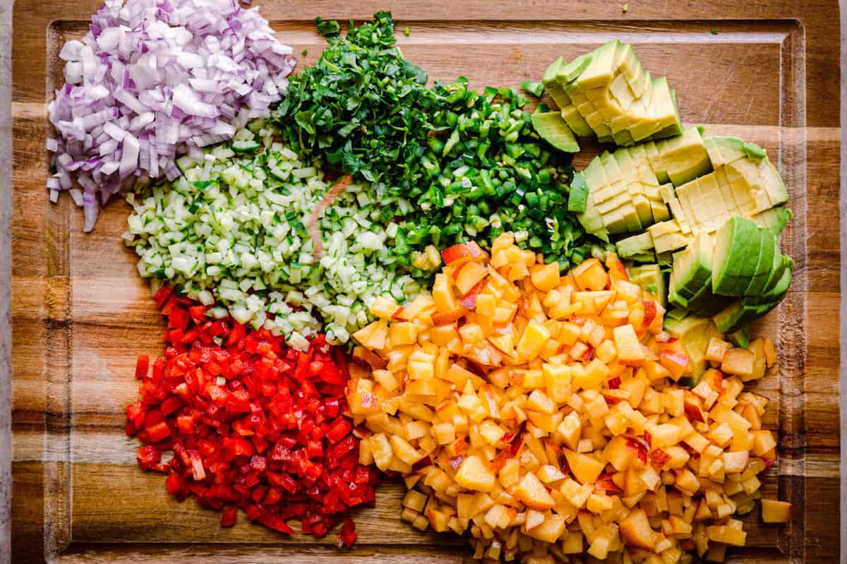 ingredients for peach avocado salsa arranged on a wooden cutting board.