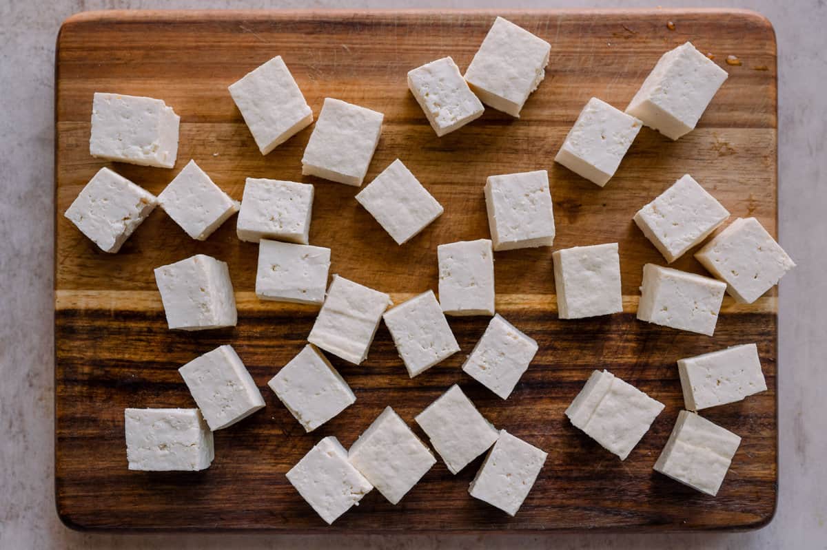 tofu cubes on a wooden cutting board.