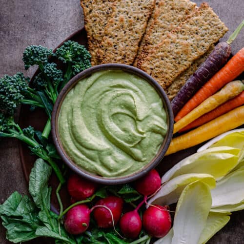cilantro cashew cream dip in a bowl surrounded by crudites and crackers.