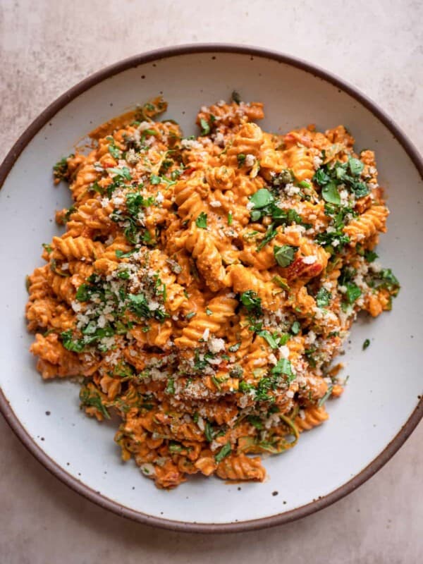 vegan roasted red pepper pasta salad in a speckled white bowl, garnished with basil.