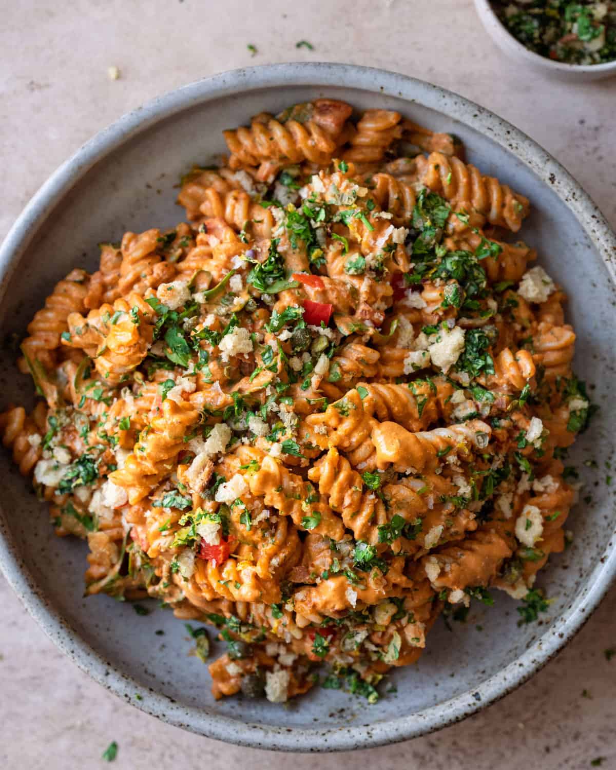roasted red pepper pasta with arugula in a gray bowl on light pink surface. 