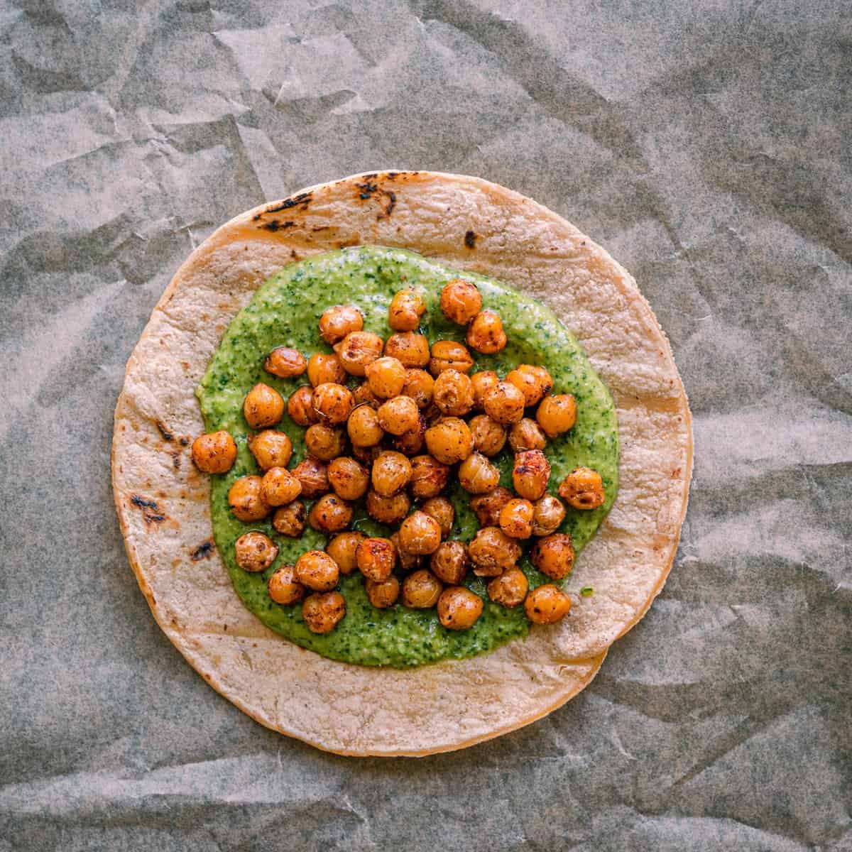 assembling tacos - charred corn tortilla with cilantro pesto and spiced chickpeas on top