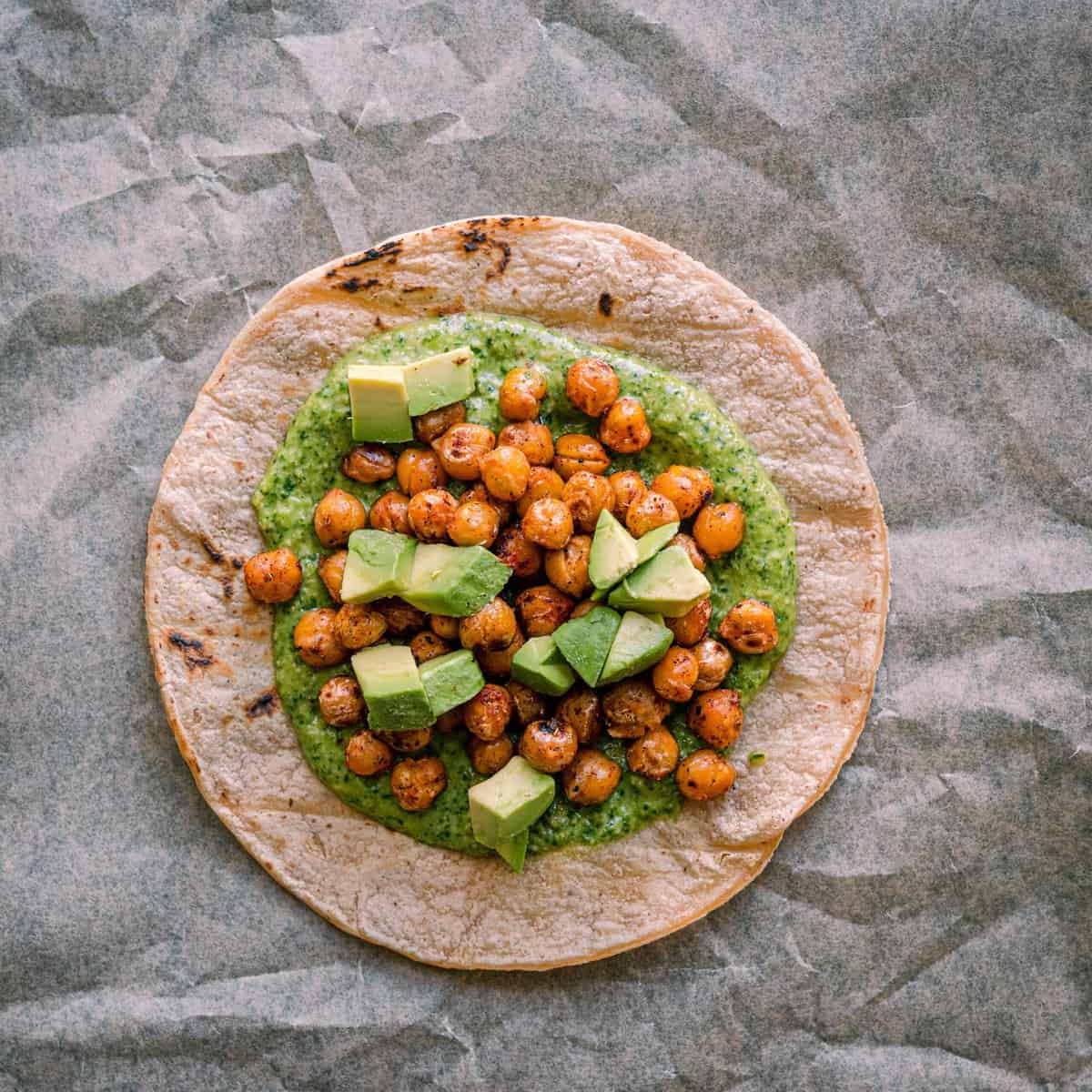 assembling tacos - charred corn tortilla with cilantro pesto, spiced chickpeas, and avocado on top