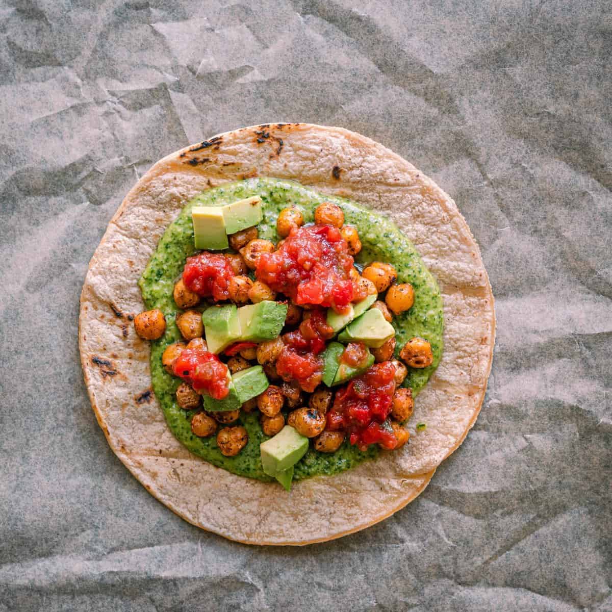 assembling tacos - charred corn tortilla with cilantro pesto, spiced chickpeas, avocado, and salsa on top