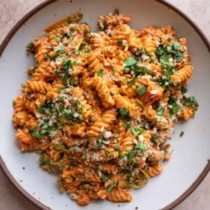 vegan roasted red pepper pasta salad in a speckled white bowl, garnished with basil.