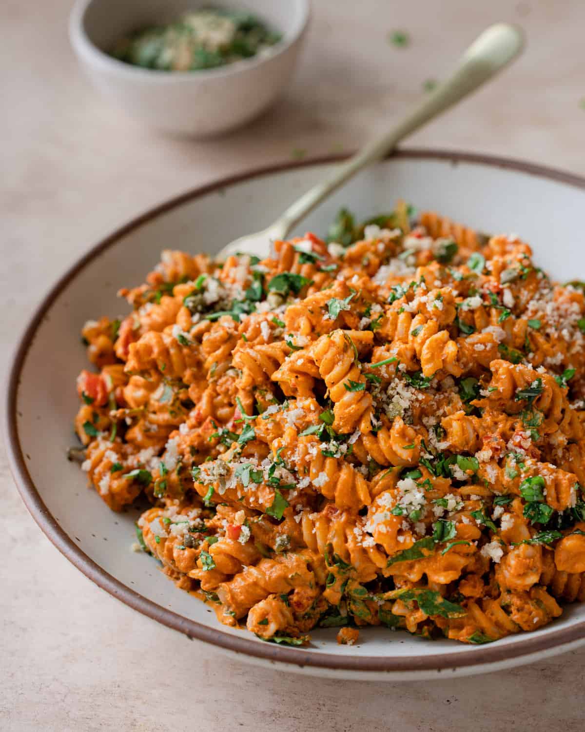 side angle of vegan roasted red pepper pasta, garnished with basil topping in white bowl.