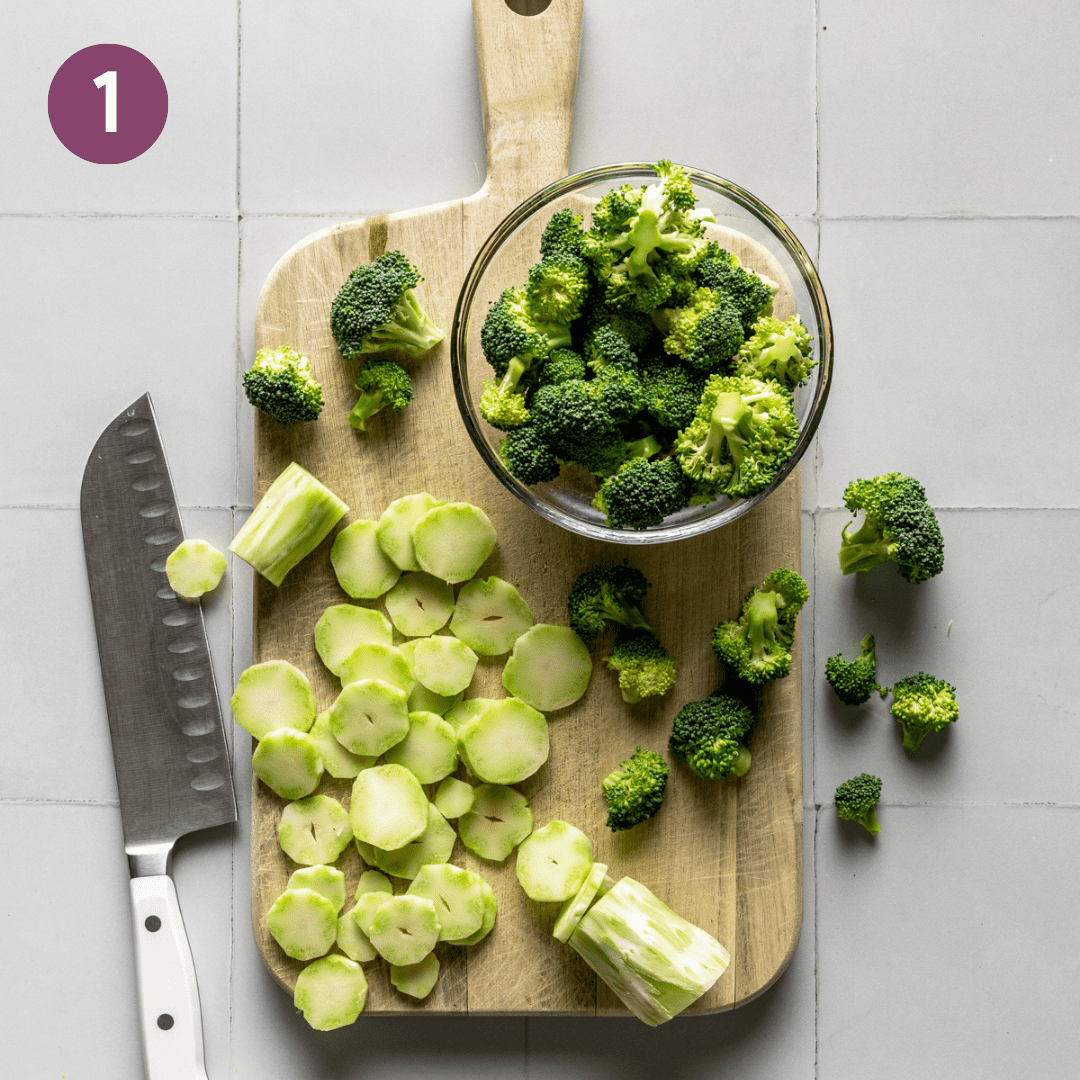 broccoli florets in a bowl and broccoli stalks being sliced into coins on wooden cutting board. 