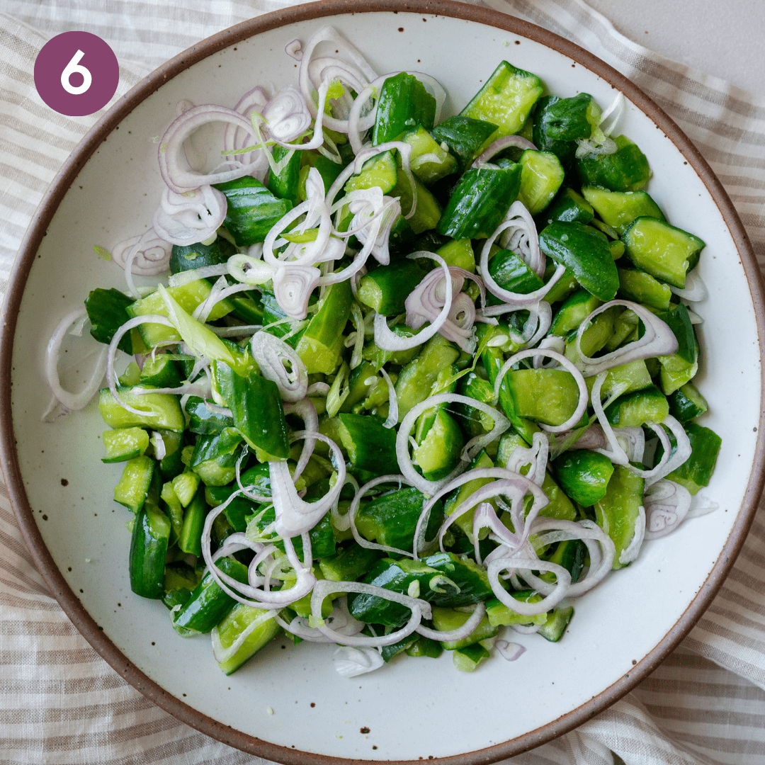 smashed cucumbers, shallots and scallions in a white speckled bowl on a linen napkin.