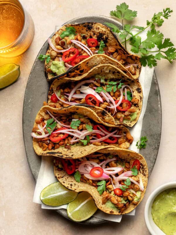 Four tempeh tacos garnished with cilantro and lime on a platter.