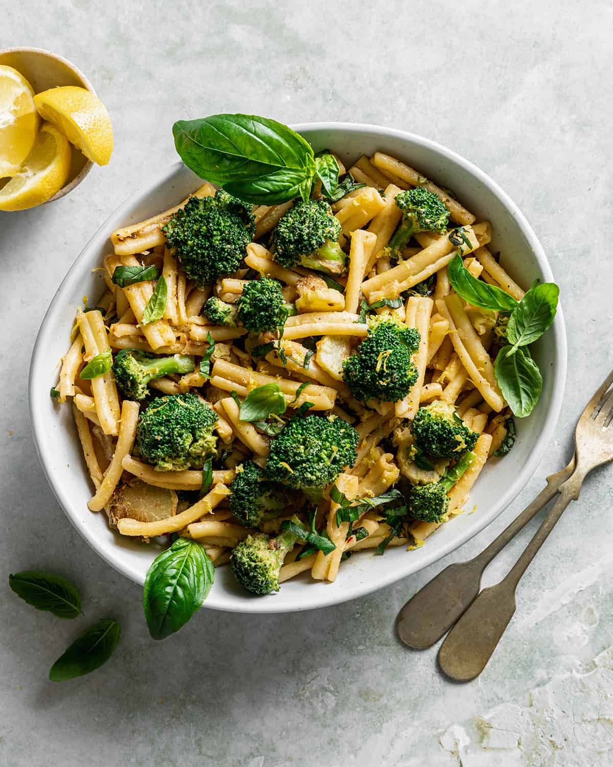 a ceramic bowl filled with tahini pasta and broccoli topped with basil on a marbled surface.