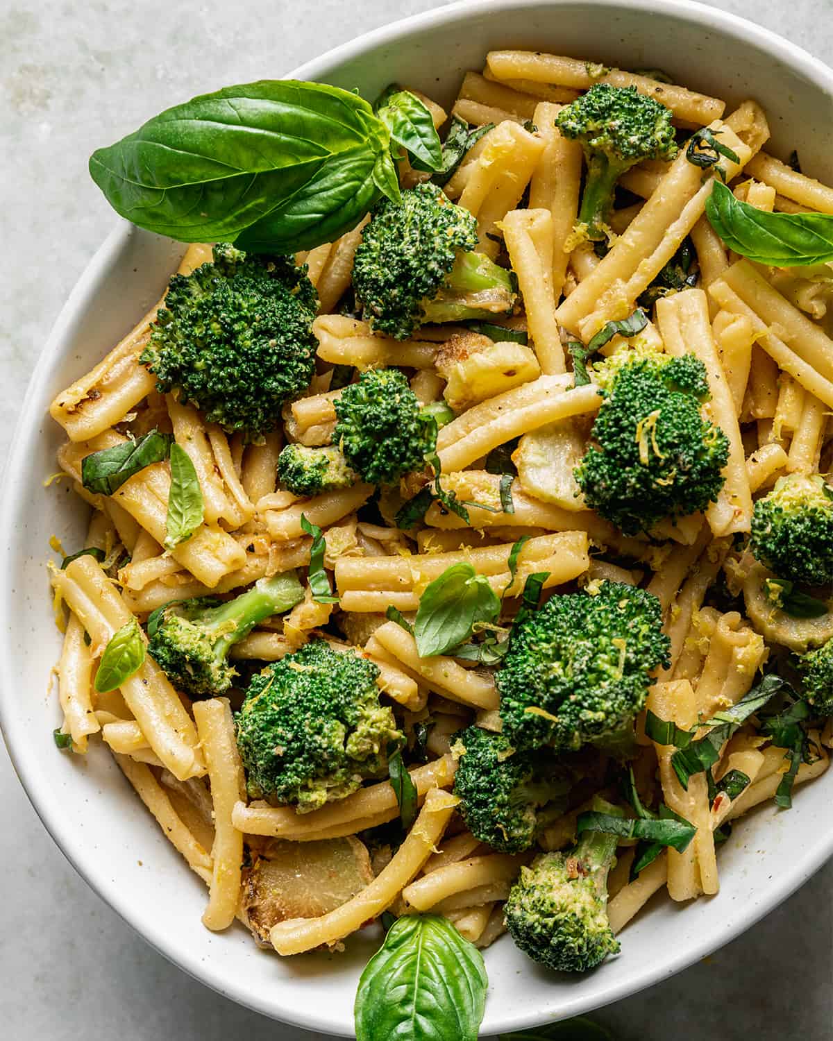 closeup of tahini pasta with broccoli, topped with basil, in a ceramic bowl.