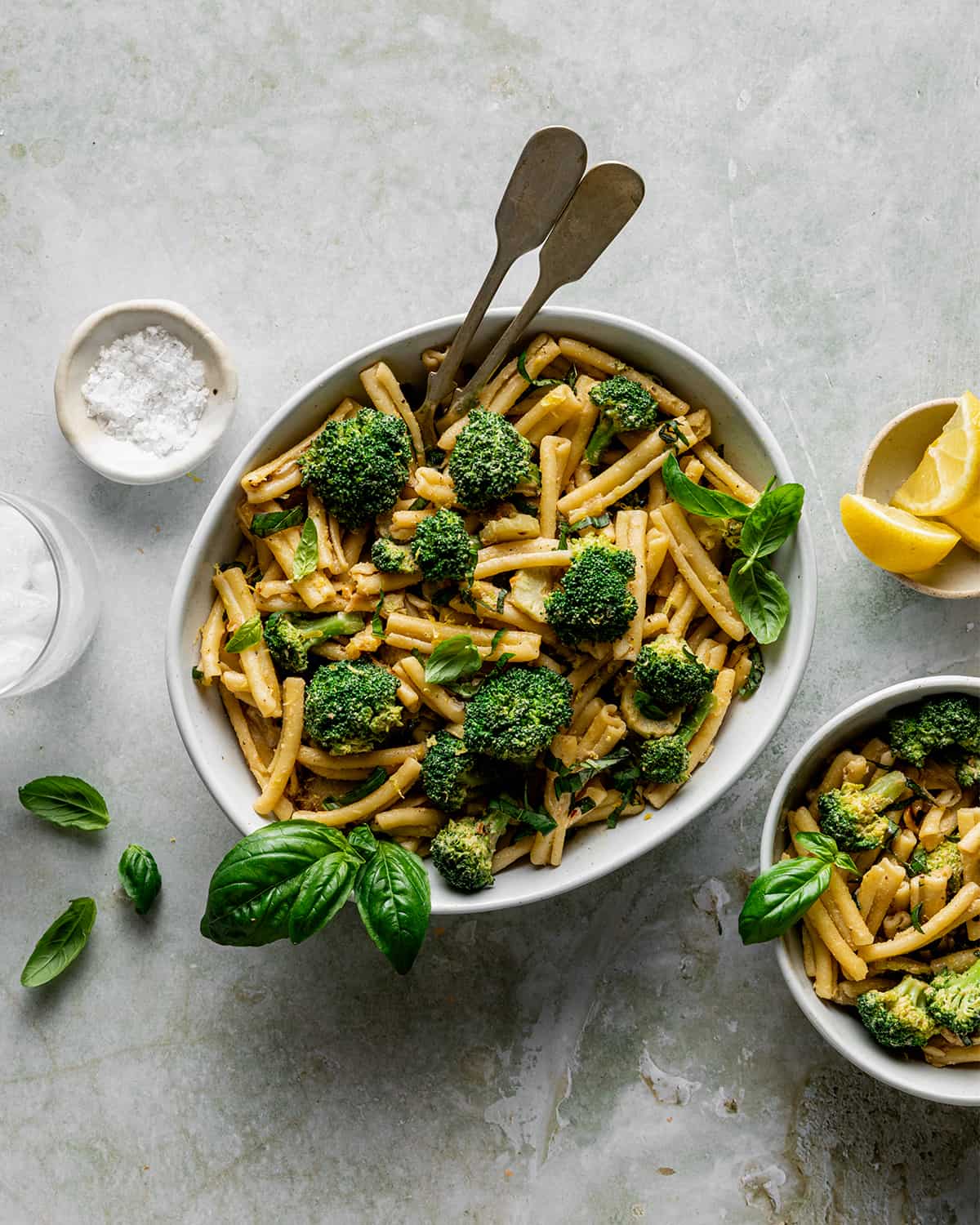 large bowl of tahini pasta with broccoli and basil, with small bowl and glass of water.