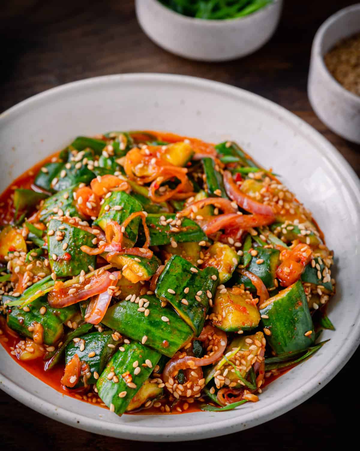 spicy cucumber salad with shallots in a white bowl on wooden surface. 