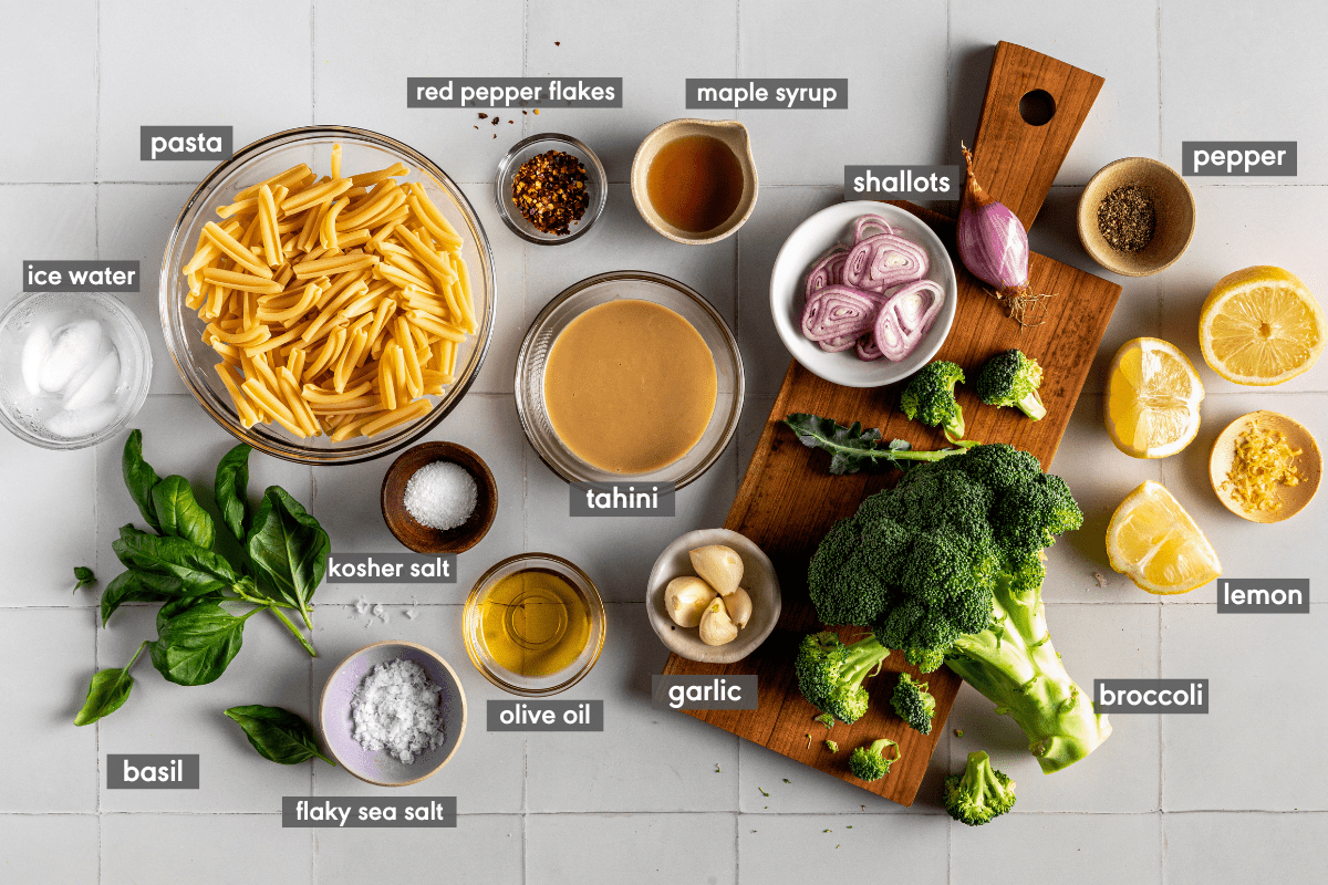ingredients for tahini pasta laid out on white tiled surface with ingredient labels. 