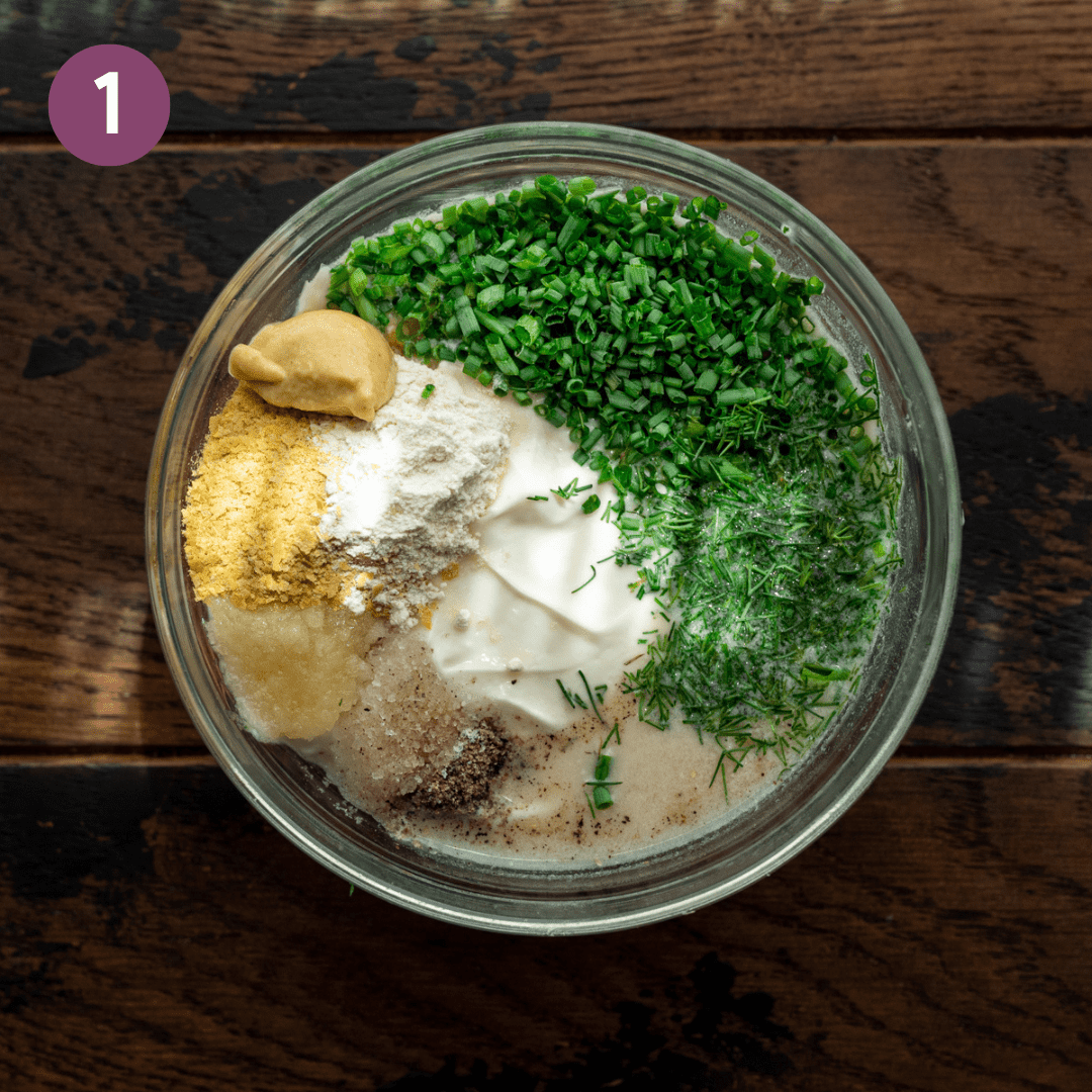 vegan mayo, chopped chives and dill, mustard, and nutritional yeast in a bowl on a wooden table.