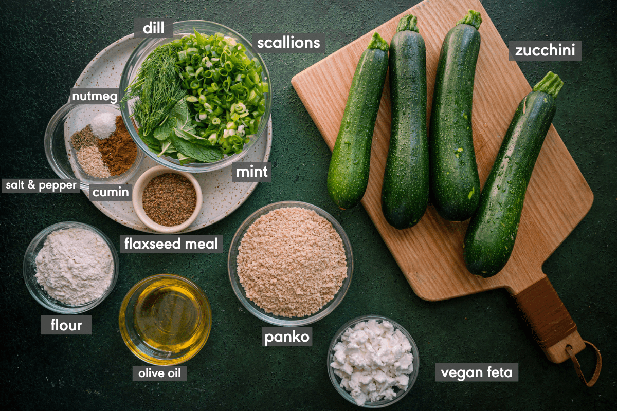 ingredients for vegan zucchini fritters laid out on a green table with ingredients labeled. 