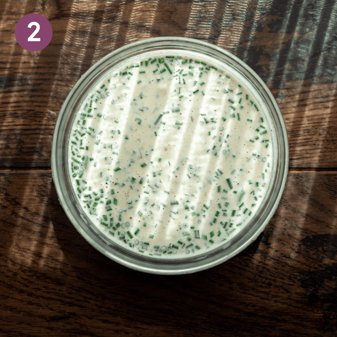 vegan ranch dressing with chives in a glass bowl on a wooden table in morning light.