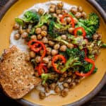 Broccoli and chickpea dish with bread on a yellow plate on a wooden table.