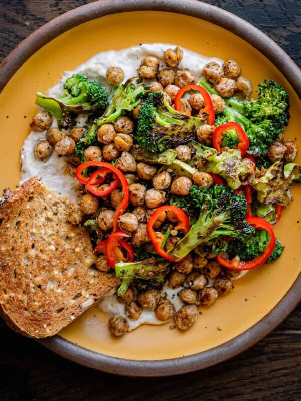 Broccoli and chickpea dish with bread on a yellow plate on a wooden table.
