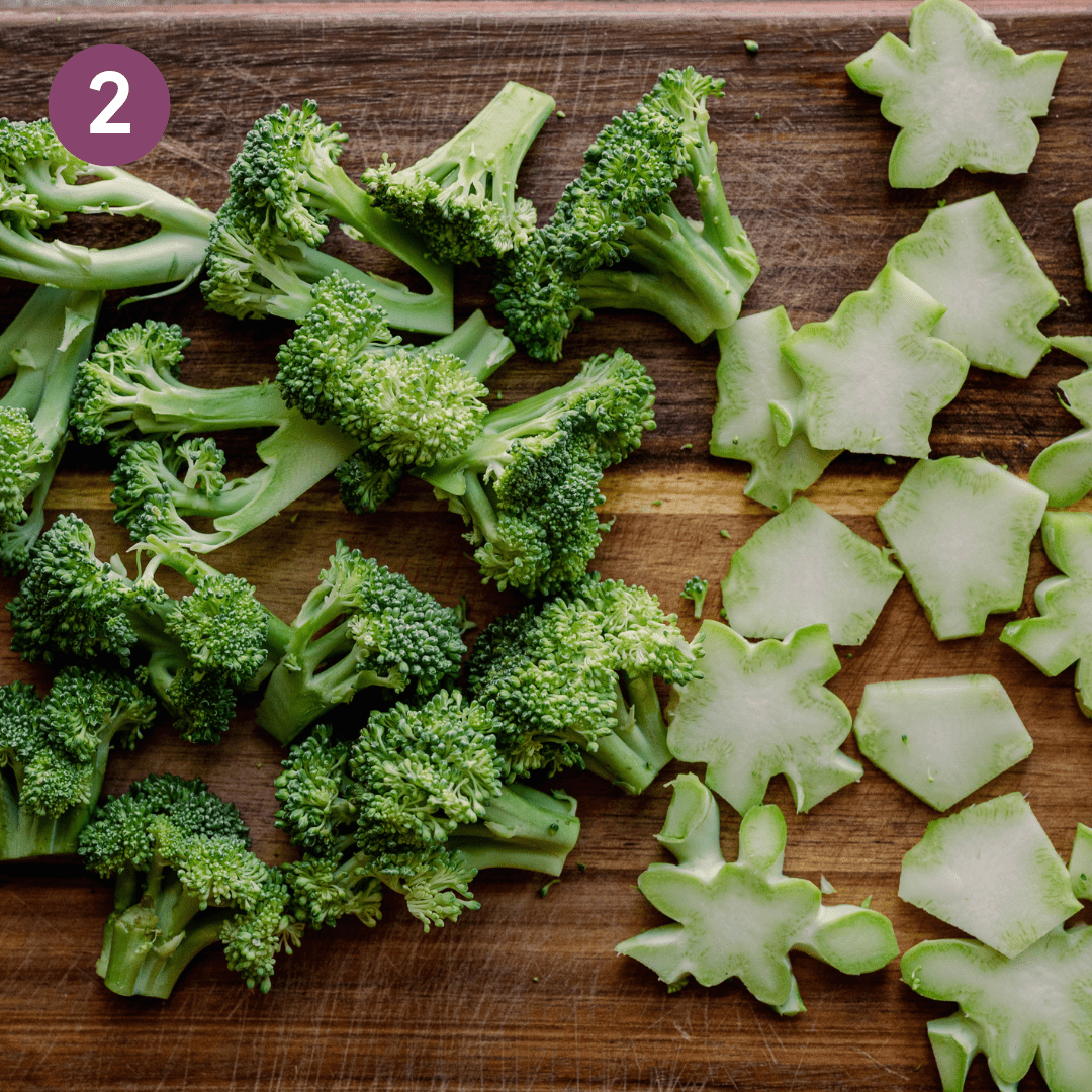Raw broccoli florets and sliced broccoli stems on a large wood cutting board.