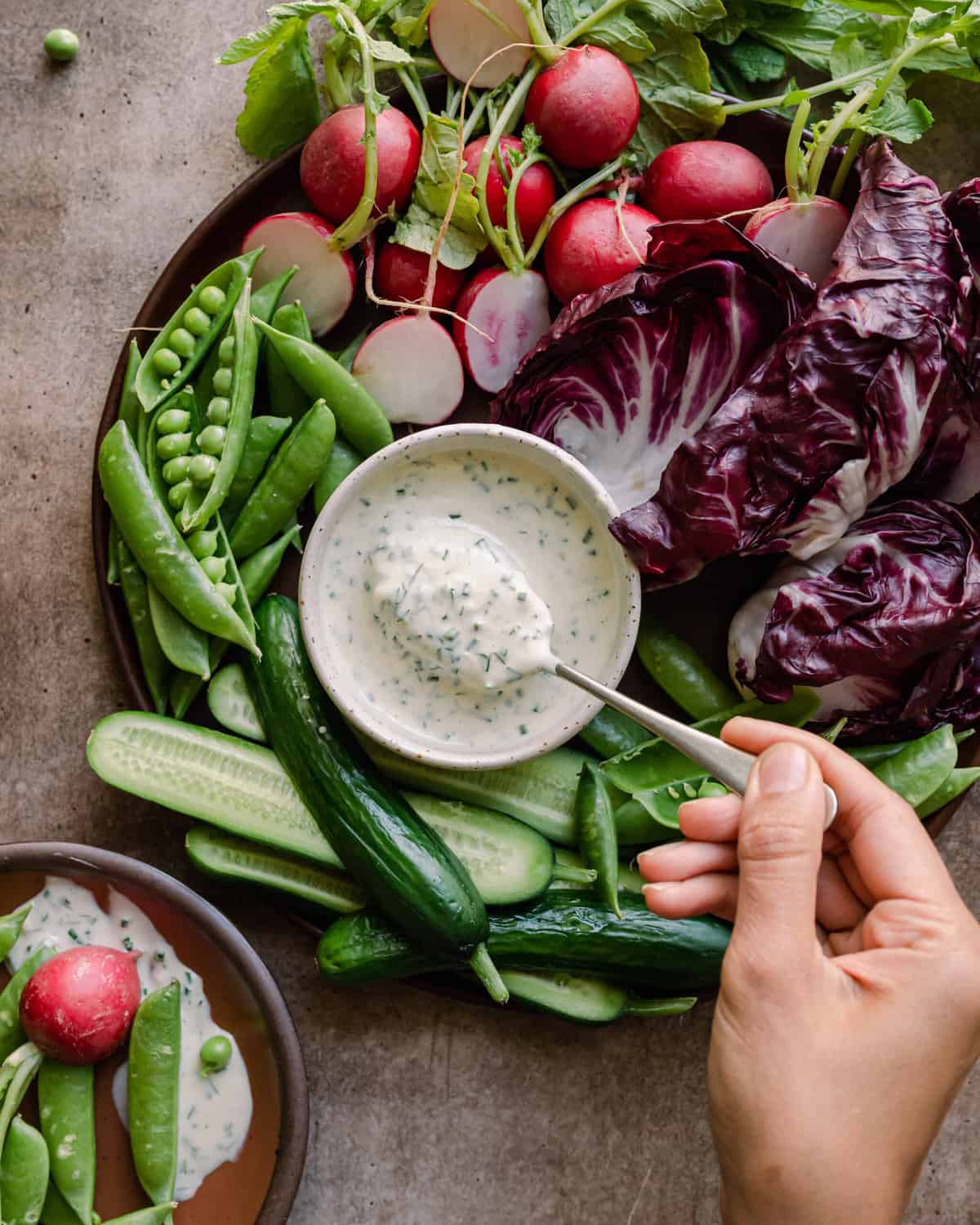 woman's hands dipping a spoon into bowl of vegan ranch dressing surrounded by crudites platter. 