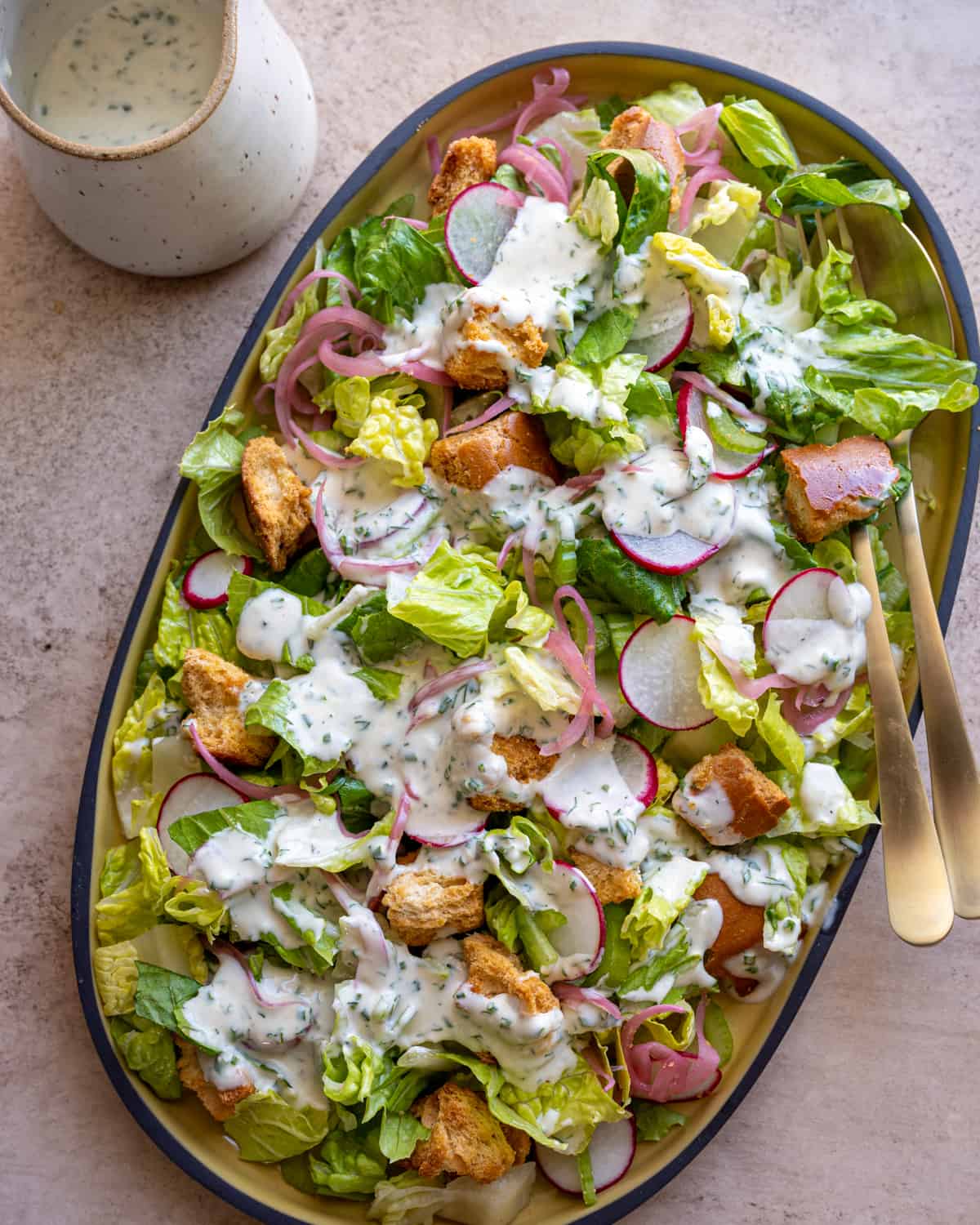 vegan ranch dressing drizzled over romaine salad with pickled radishes and croutons on yellow platter.