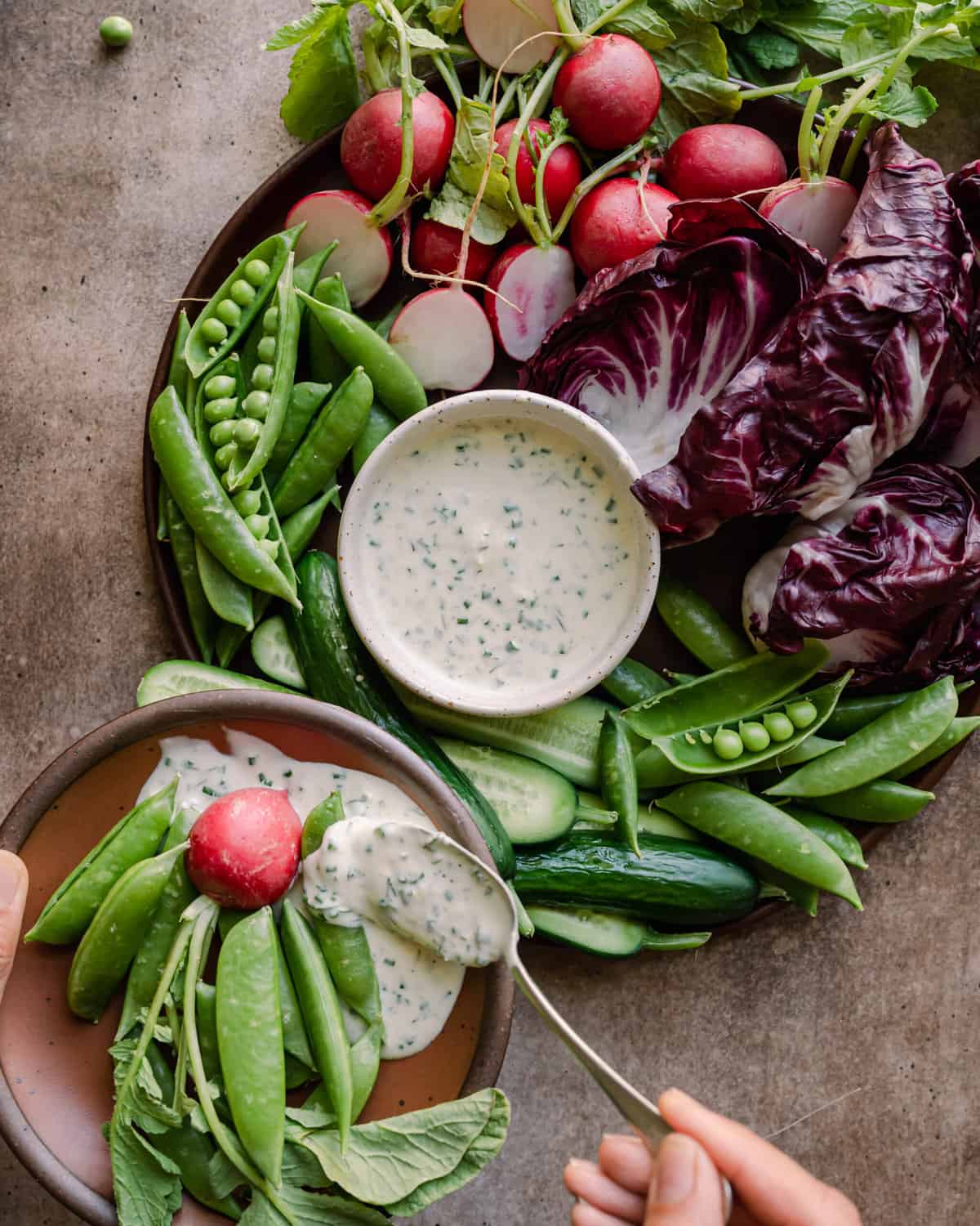 woman's hands spooning vegan ranch dressing onto small plate next to crudites platter. 
