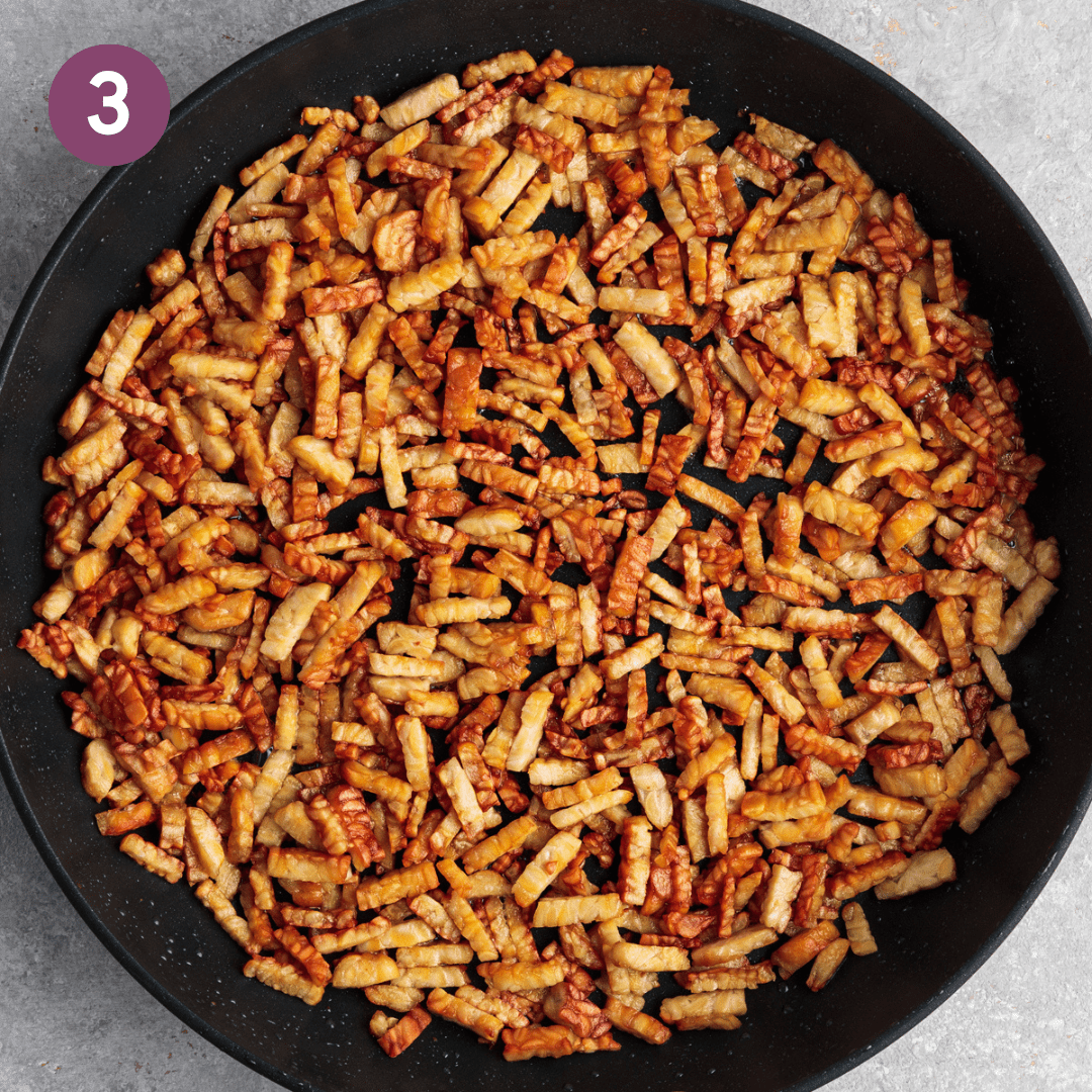 Browned thinly sliced tempeh in a black frying pan.