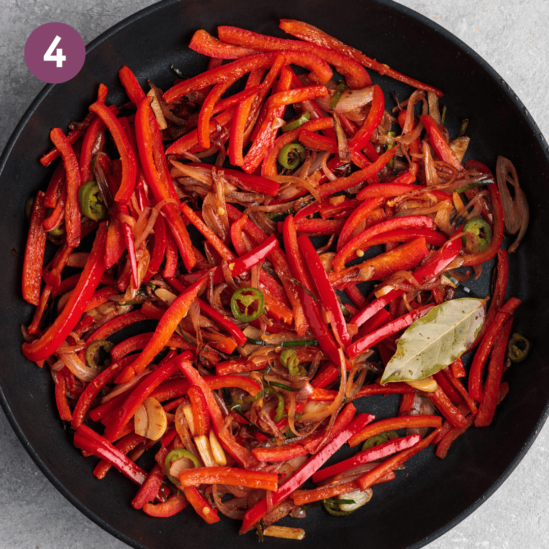 Bell peppers added to cooked aromatics in a black frying pan.