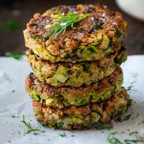 a stack of four vegan zucchini fritters on parchment paper with herbs and tzatziki on the side.